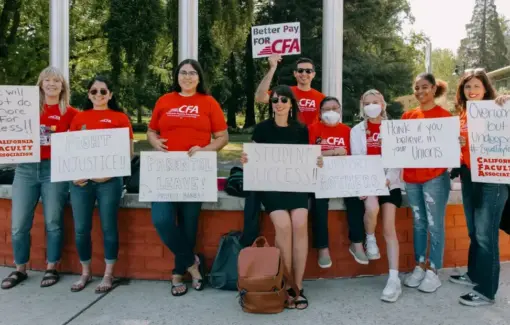 People stand in a row outside holding signs about better working conditions.