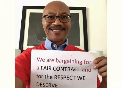 Charles Toombs holds a sign reading "We are bargaining for a fair contract and for the respect we deserve."