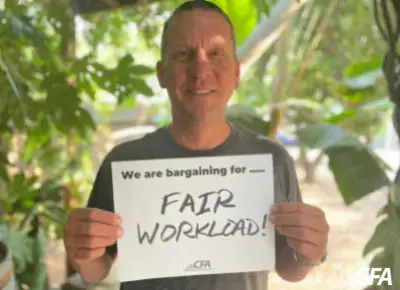 Kevin Wehr holds a sign saying "we are bargaining for fair workload."