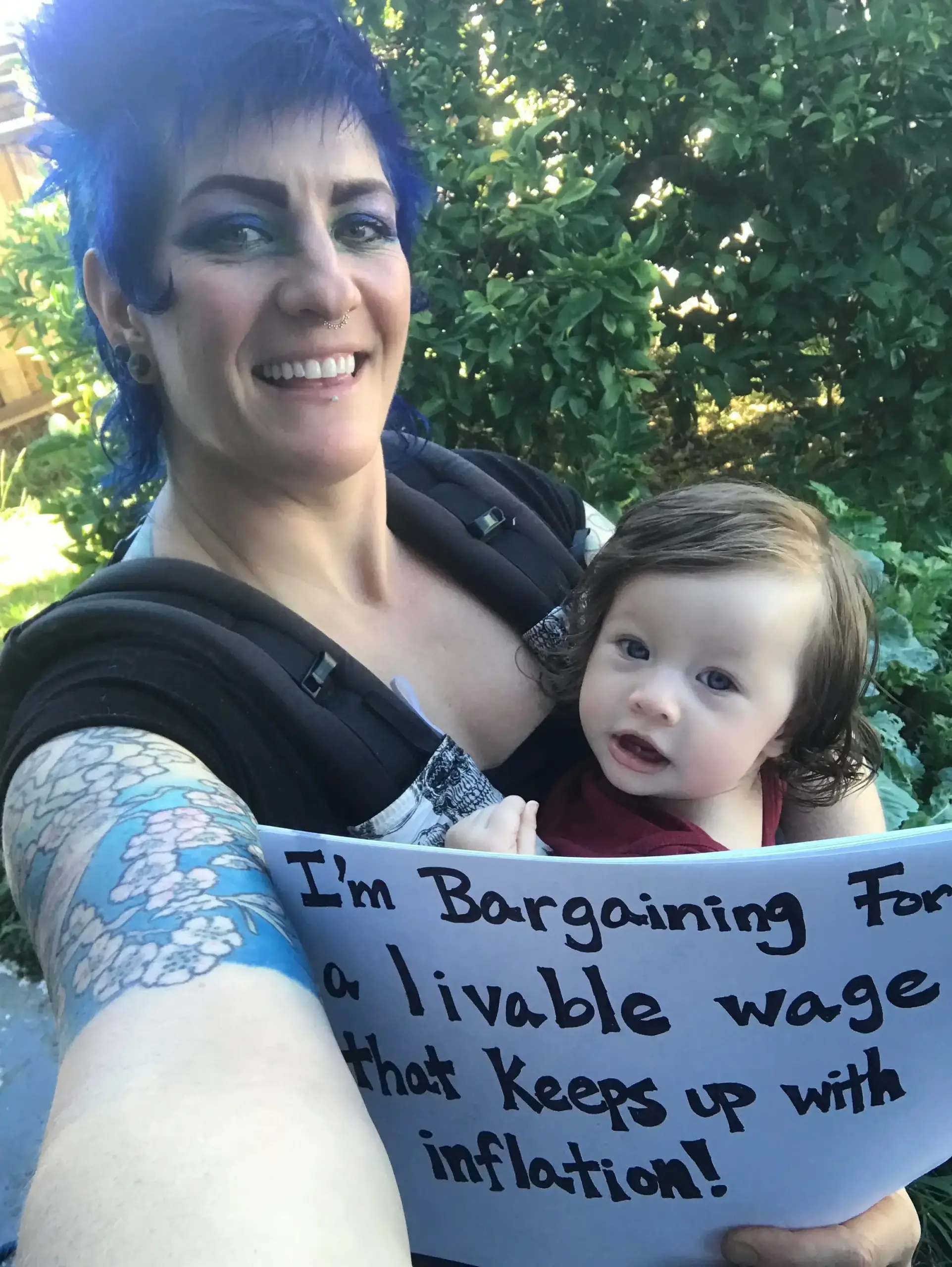 CFA member Anne Luna-Gordinier holds her baby and a sign saying "I'm bargaining for a livable wage that keeps pace with inflation!"