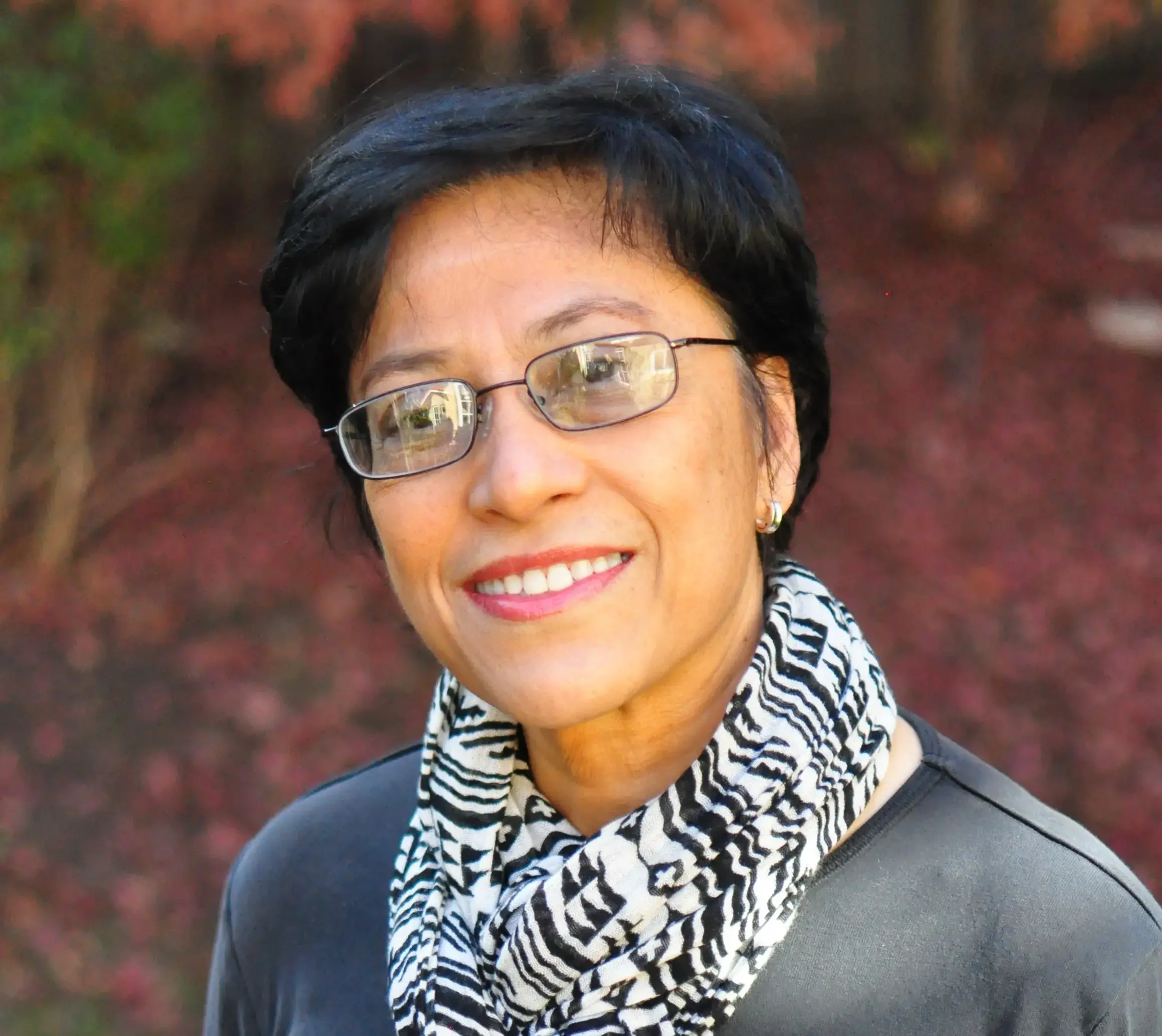 Woman with glasses wearing a gray shirt and patterned scarf smiling for a picture.
