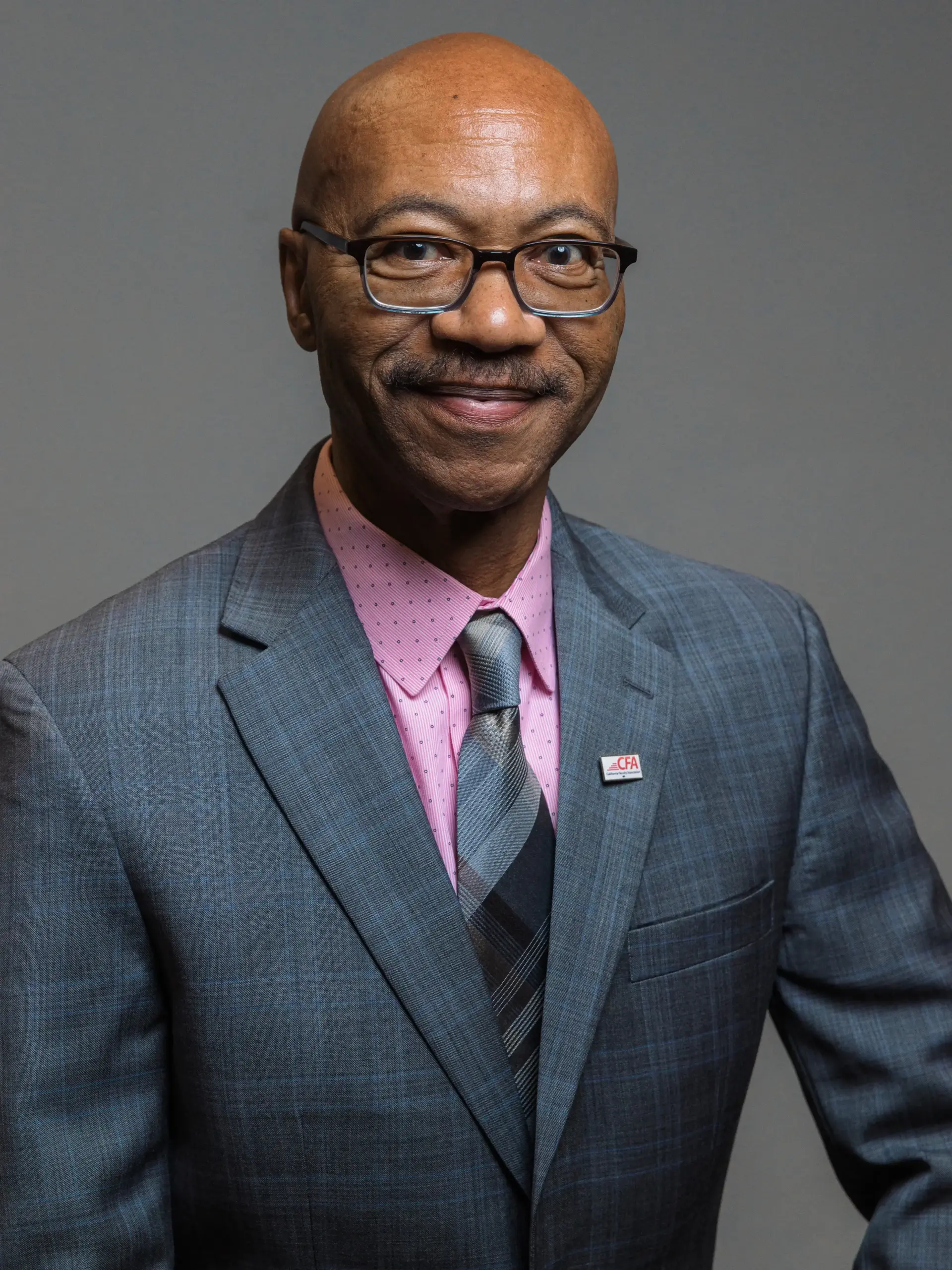 Charles Toombs posing with a purple dress shirt and gray tie and suit jacket.