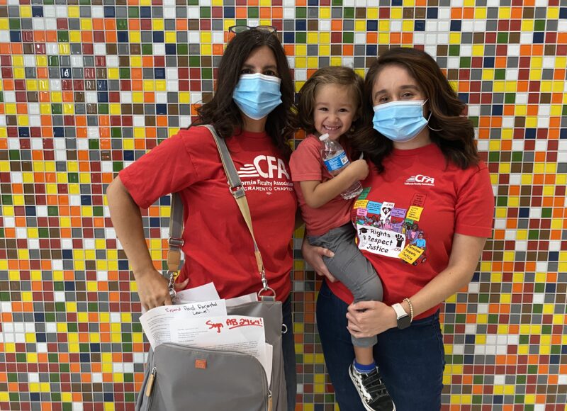 Two women holding a child and diaper bag stand for a photo.