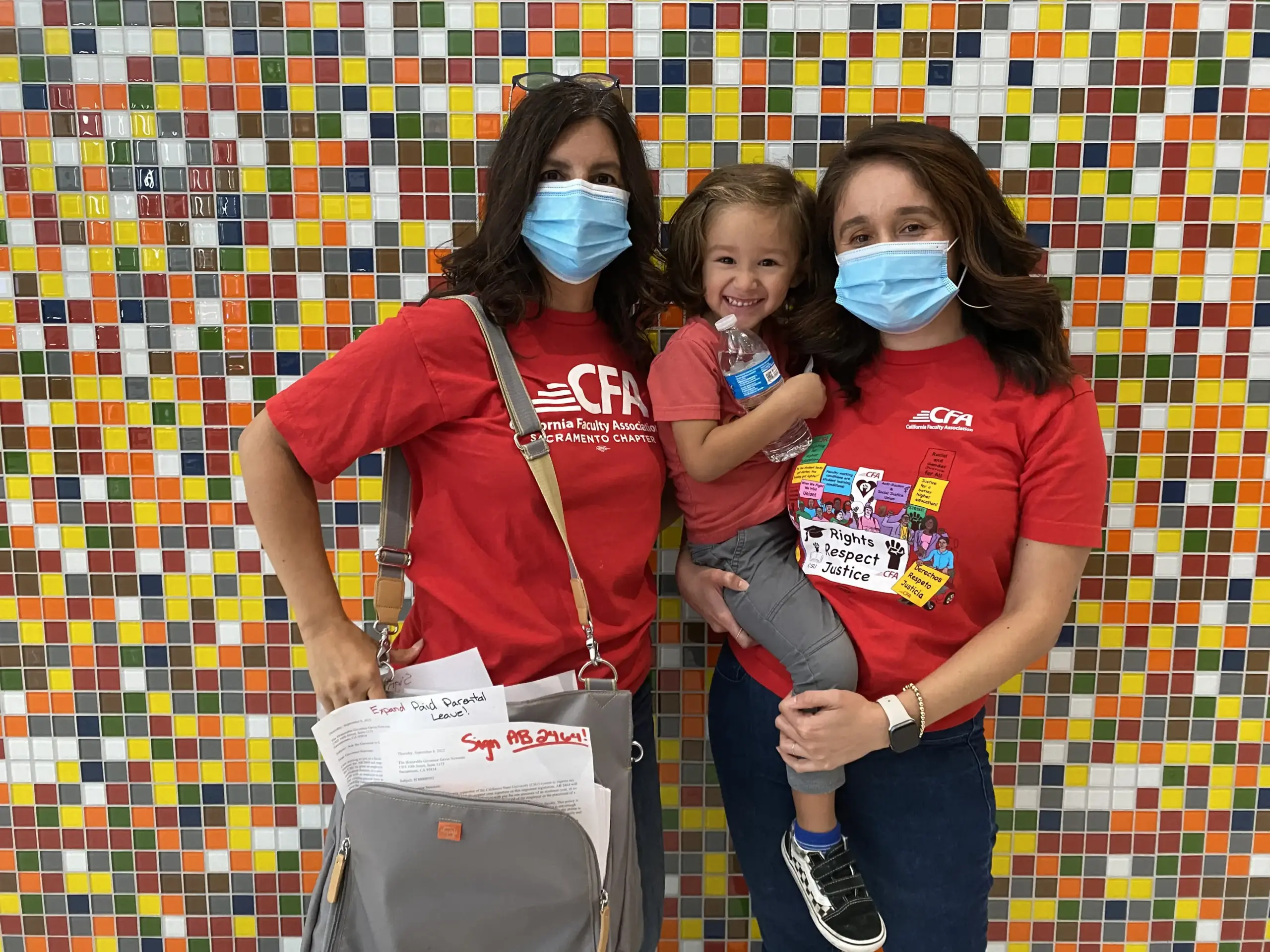 Two women holding a child and diaper bag stand for a photo.