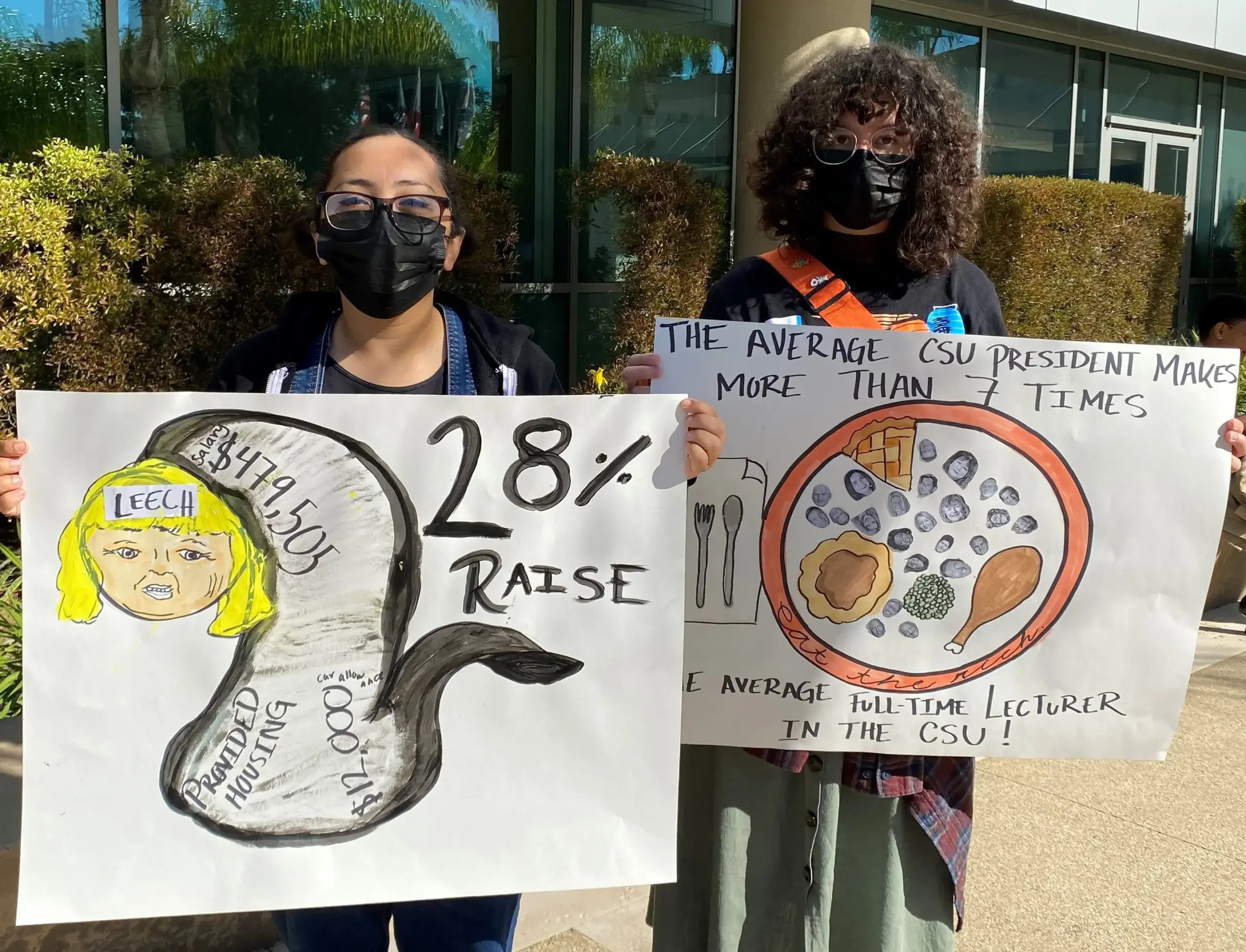 Two students with masks stand with signs outdoors.