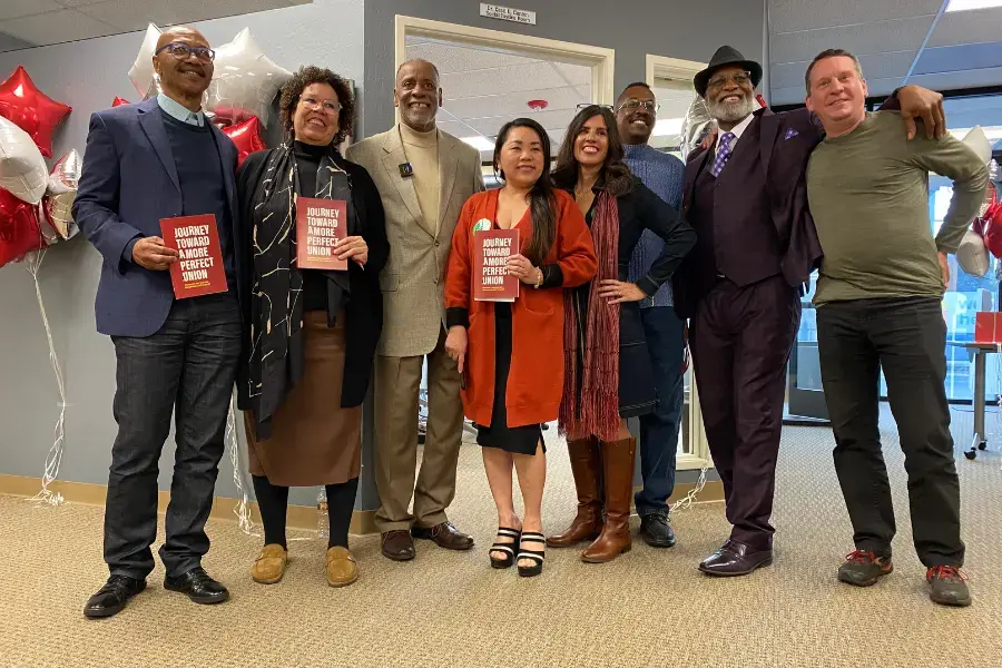 Eight people stand together for a photo next to a conference room.