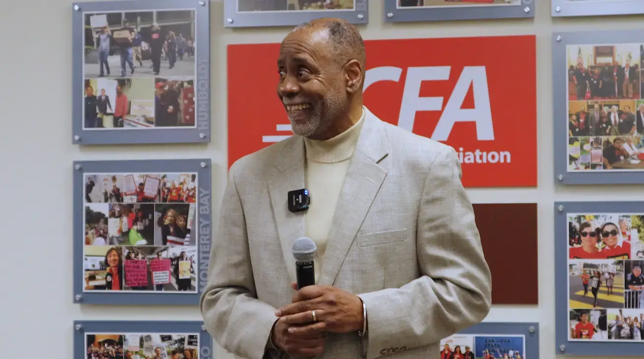 Cecil Canton in a light brown suit speaks with a microphone in front of a photo collage.