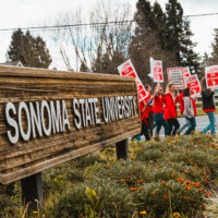 Faculty on strike at E.Cotati Ave main SSU entrance with Sonoma State University sign in foreground.