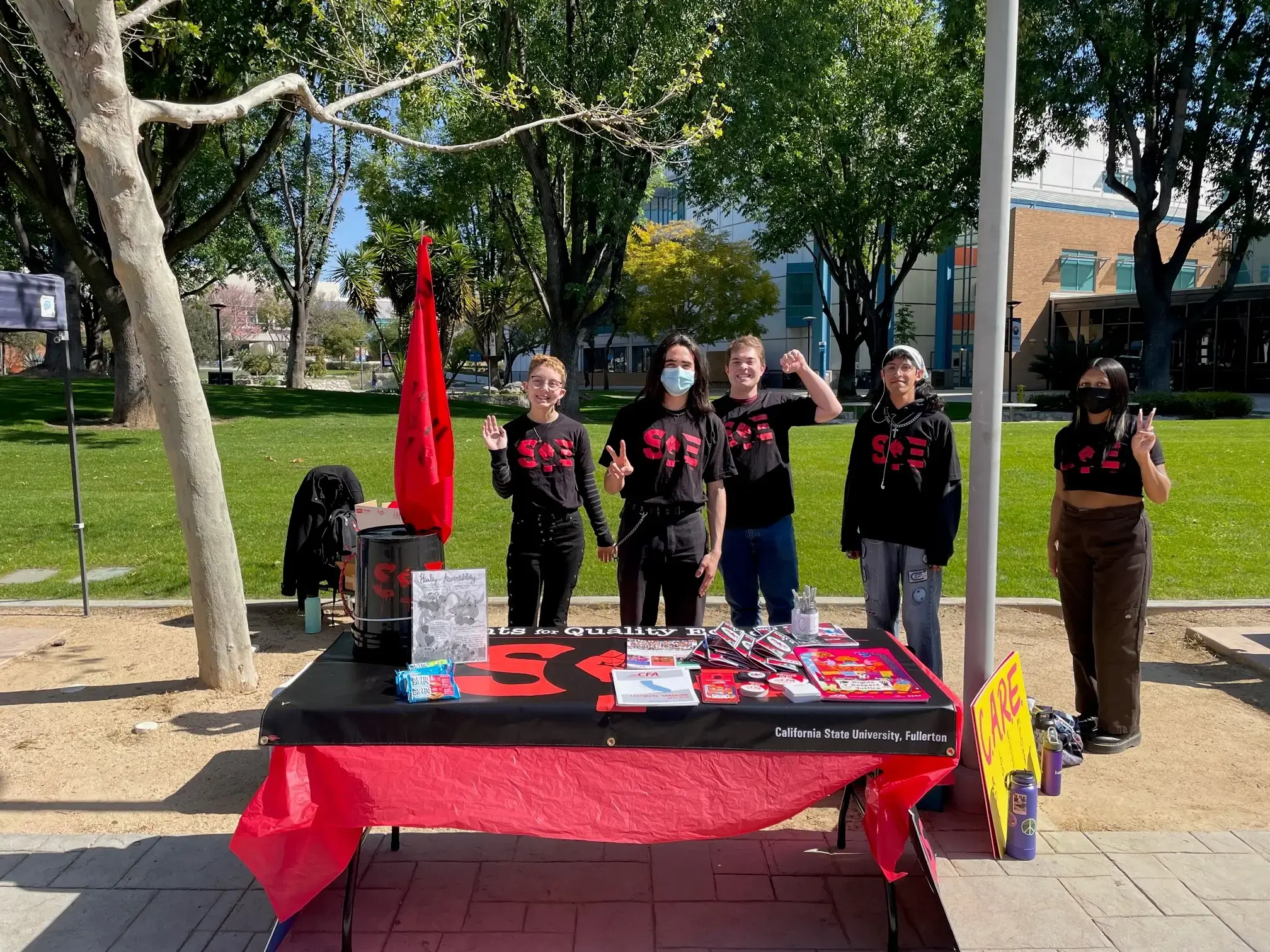 Students in SQE shirts outdoors tabling at a campus.