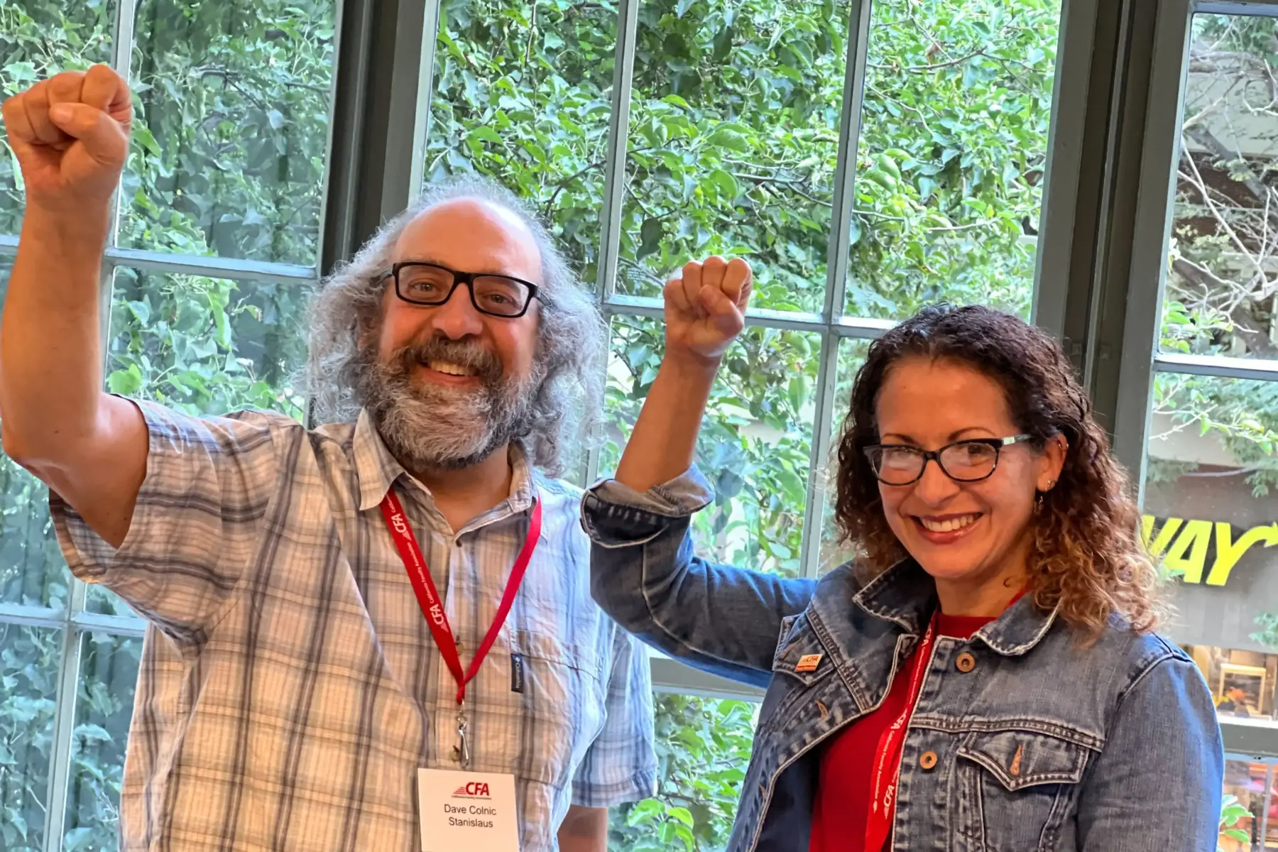 Two people standing by a window pose with raised fists