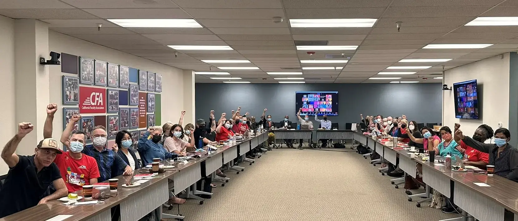 Conference room full of members holding their fists in the air and wearing face masks.