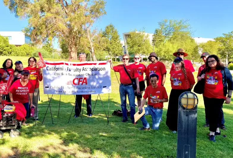 Members in red t-shirts stand around a banner outside.