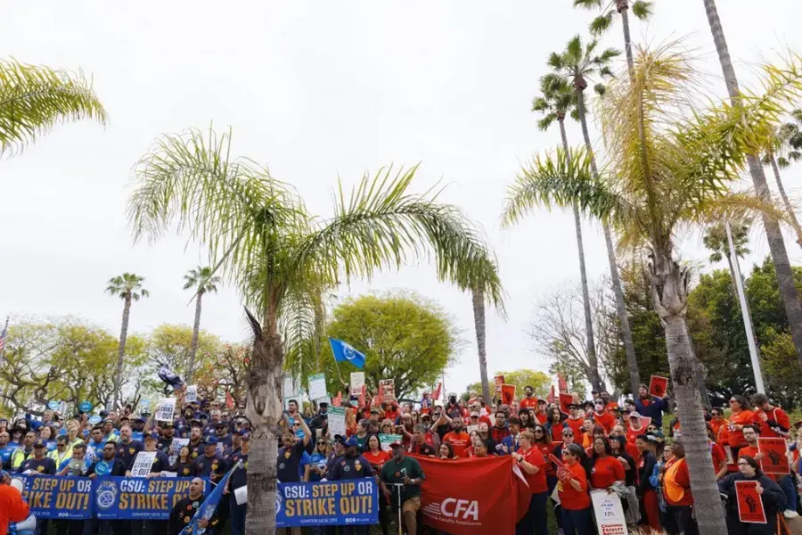 Hundreds of faculty, staff, and students are gathered together and chanting at a rally.