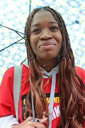 A student is wearing red and holding an umbrella over her head.