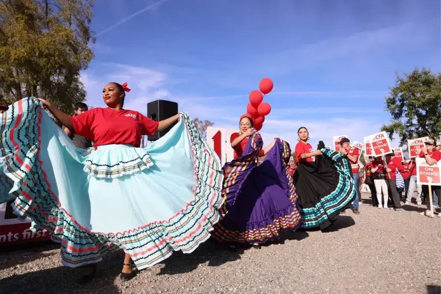 Student dancers hold up their brightly colored dresses as they dance at a rally.