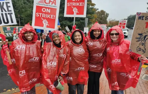 A group of pose holding picket signs and wearing red ponchos pose.