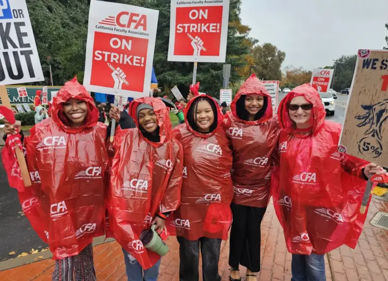 A group of pose holding picket signs and wearing red ponchos pose.