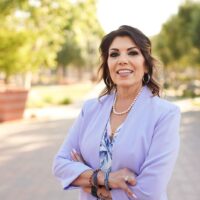 candidate wearing a lavendar blazer and pearl necklace with arms crossed