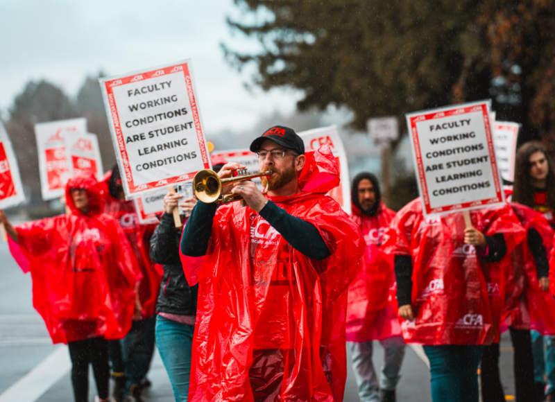 A group of people rallying outside and a person playing the trumpet.