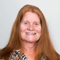 Nena Torrez from the College of Education is smiling facing the camera. She has ginger hair, blue eyes, wearing a patterned top and against a white background.