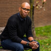 Man in black turtle neck swaeter and in glasses poses for a picture