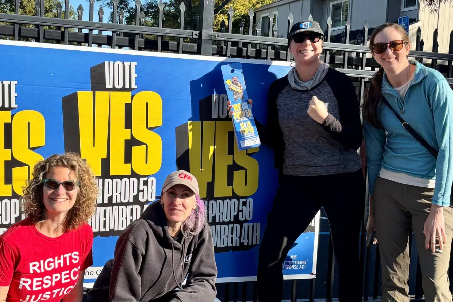Four people gather around a sign supporting Proposition 50.