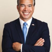 Attorney General standing with his arms crossed wearing a blue tie and black suit