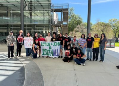 people standing outside with a banner supporting John Caravello