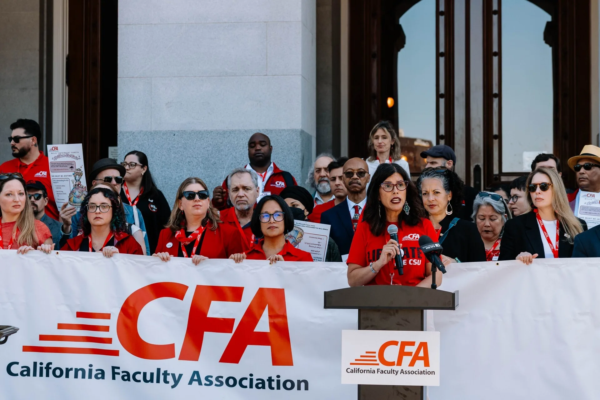 CFA President speaking at the state capital while members stand behind her with a CFA banner