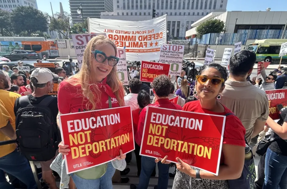 Two members in red CFA shirt with sign saying "Education Not Deportation"
