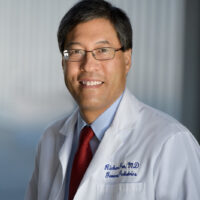 candidate in white dr coat with red tie and glasses