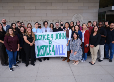 A group of people standing with a large banner "Justice $ John is Justice $ All"