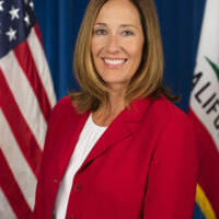 candidate in red jacket in front of US and CA flags
