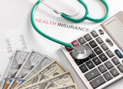 Stethoscope resting on a calculator beside a health insurance document and spread of US dollar bills.