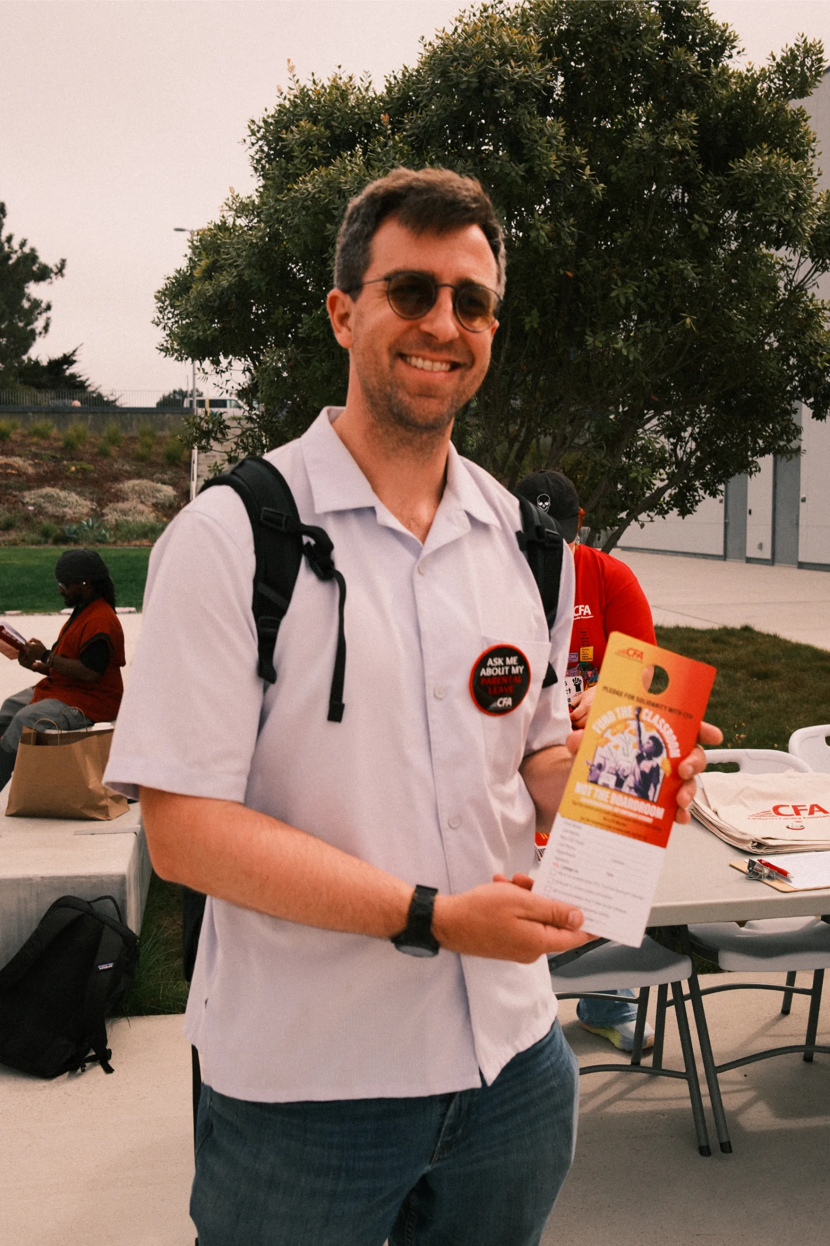 Person in sunglasses and white shirt holding a CFA pledge card