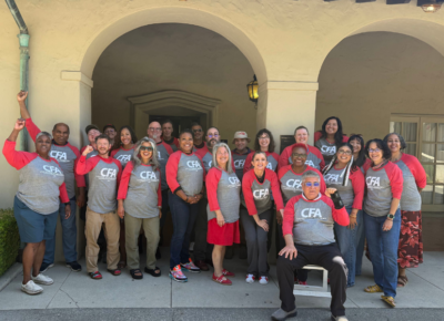 Group of diverse adults wearing matching CFA shirts posing happily under an archway outside a building.