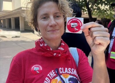 A faculty member holds up a sticker saying that she voted.