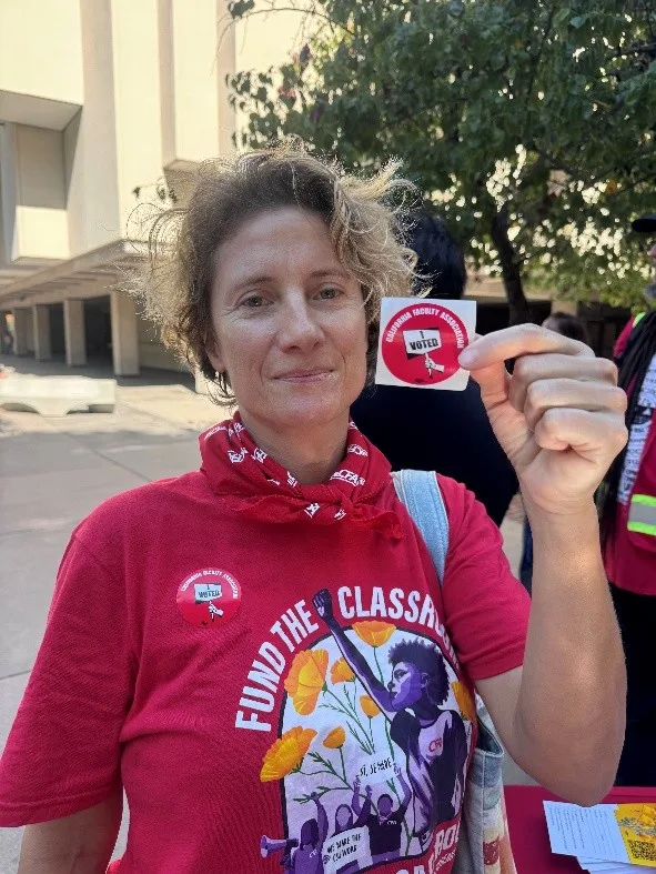A faculty member holds up a sticker saying that she voted.