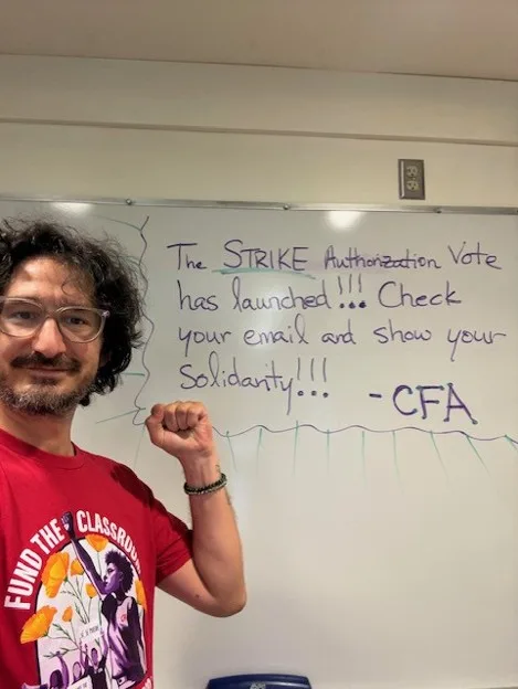 A faculty member stands in front of a a sign holding up a fist.